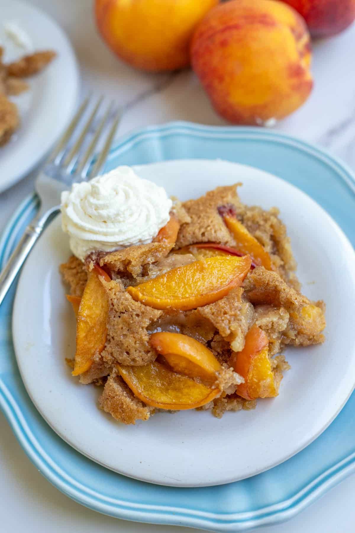 A white dessert plate filled with whole wheat peach cobbler topped with whipped cream.