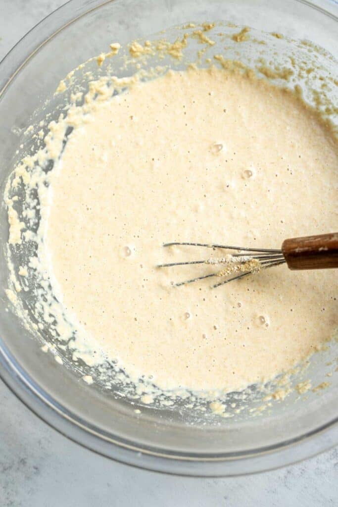 Flour, yeast, water, baking soda, sugar, and salt whisked together in a glass mixing bowl.