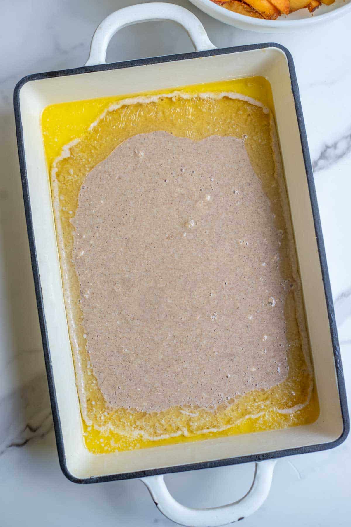 Cobbler batter poured over melted butter in a 9" x 13" pan.