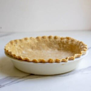 a cooked pie crust in a white pie plate on a marble counter.