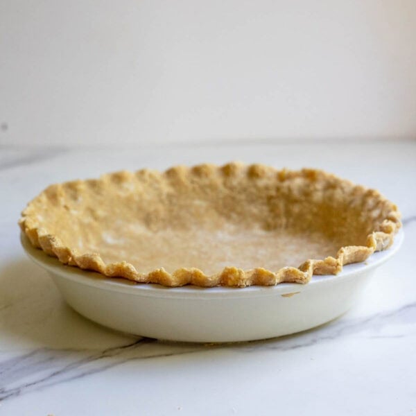 a cooked pie crust in a white pie plate on a marble counter.