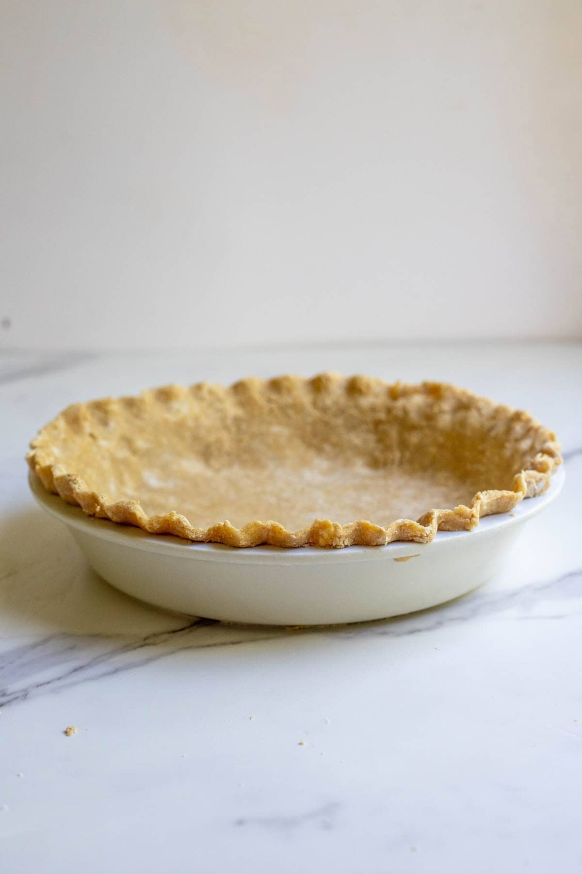 A cooked pie crust in a white pie plate on a marble counter.