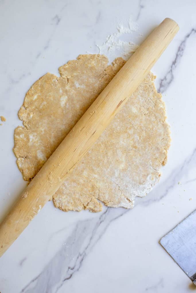 A whole wheat pie crust being rolled out on a marble countertop.