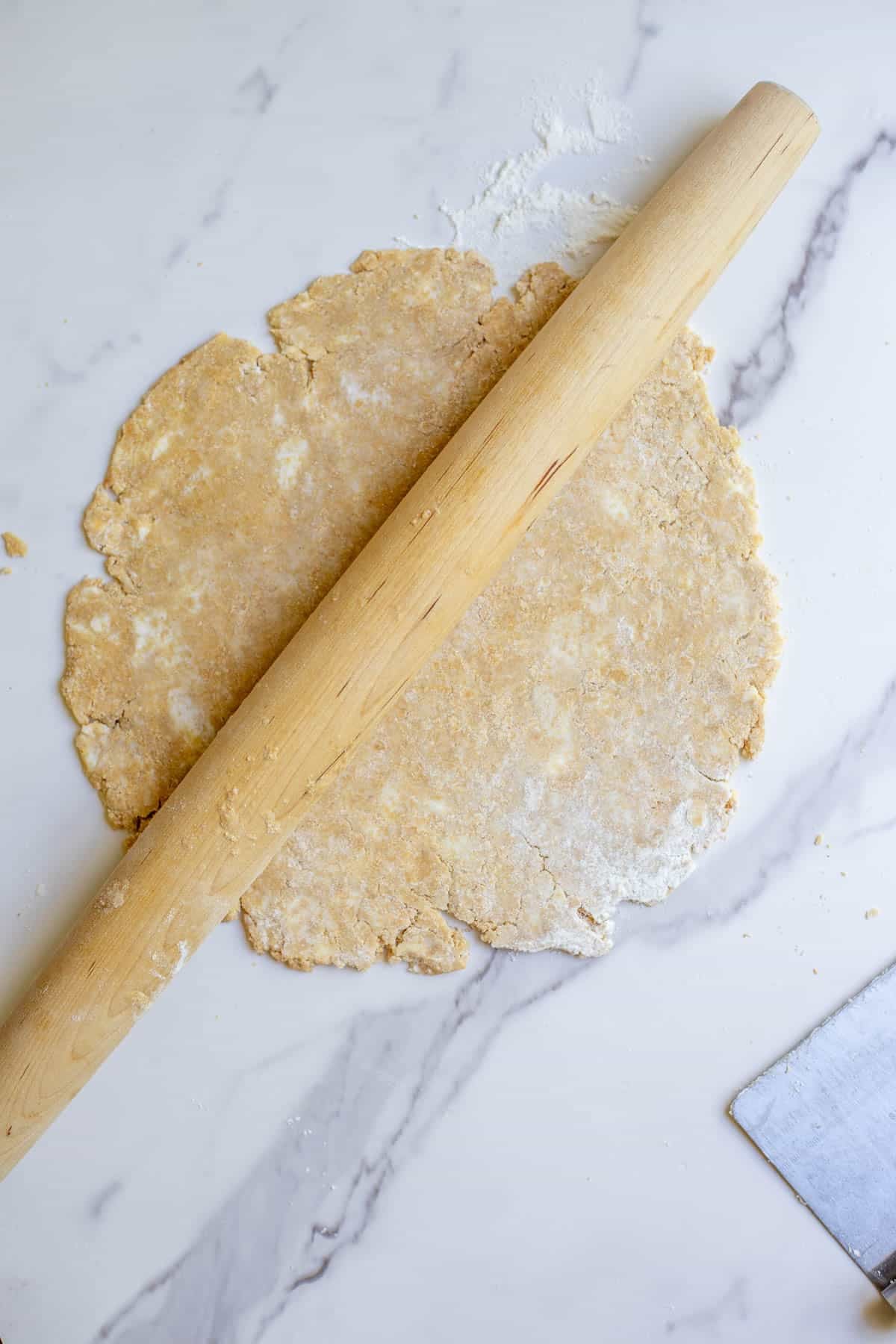 A whole wheat pie crust being rolled out on a marble countertop.