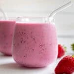 A glass with milk kefir smoothie next to a strawberry.
