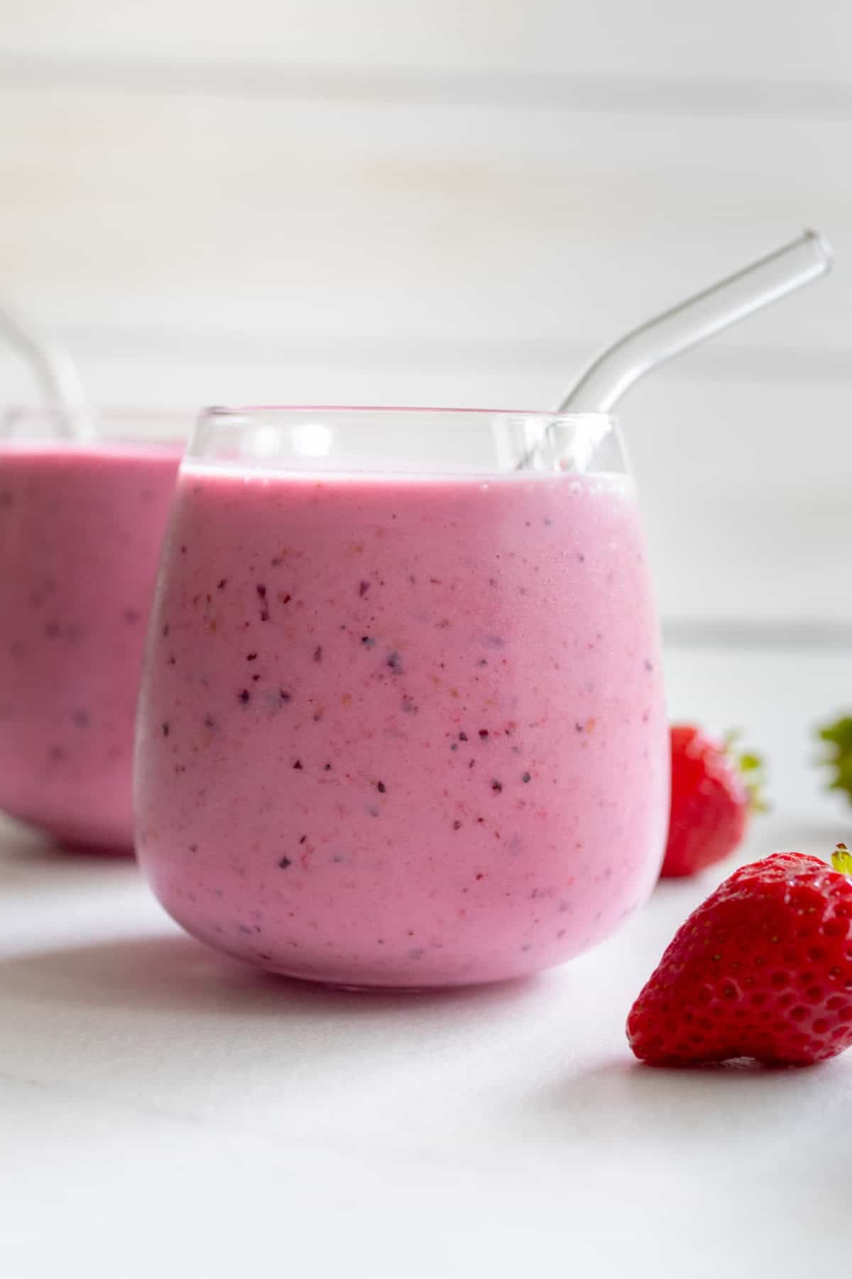 A glass with milk kefir smoothie next to a strawberry.