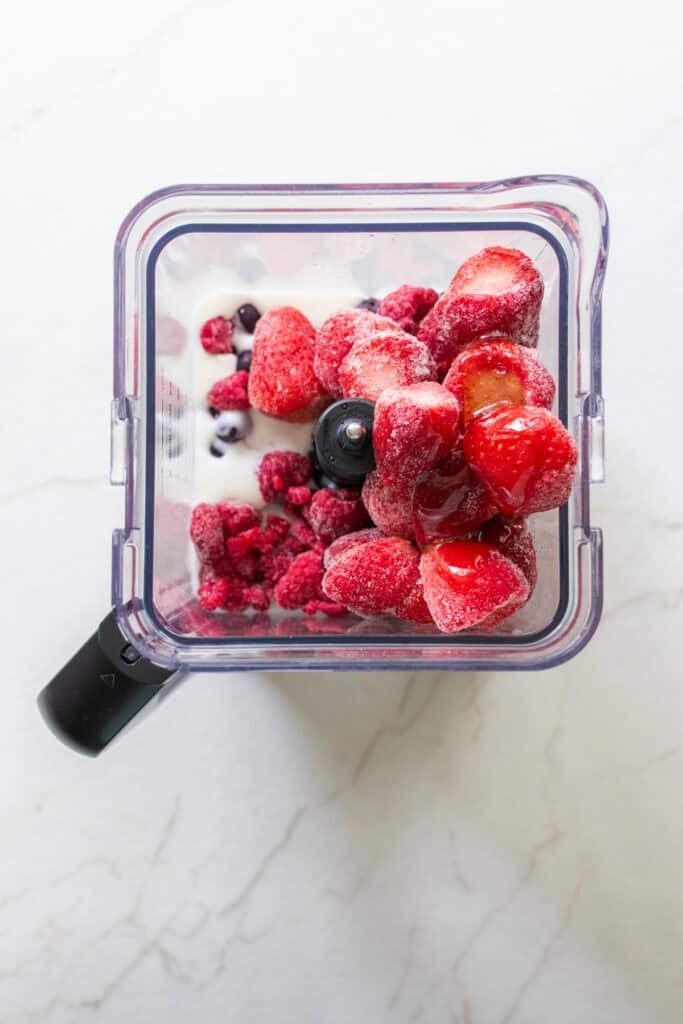 Frozen fruit added to a blender with milk kefir.