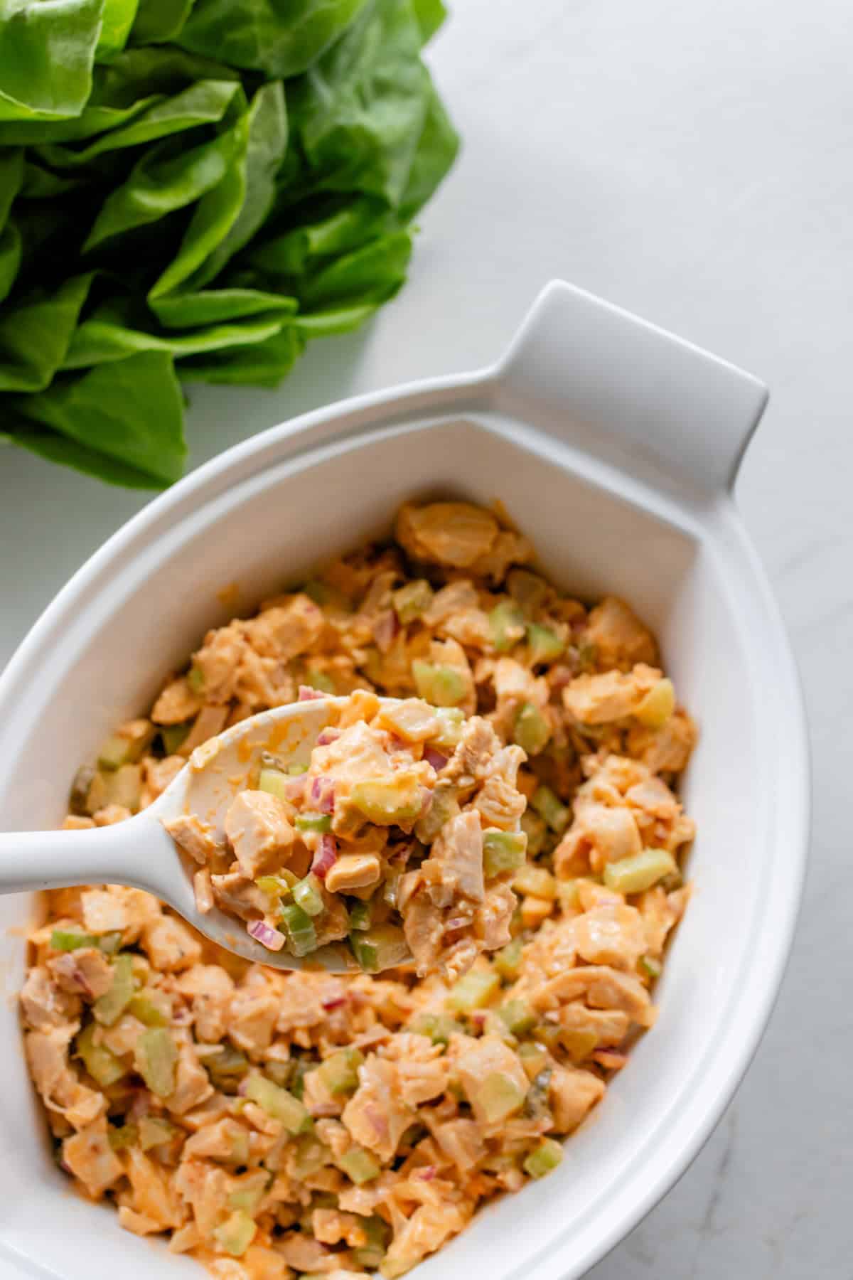 Buffalo chicken salad in a serving platter with a spoon scooping some out.