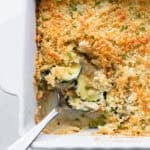 Part of a casserole dish of gratin with a silver serving spoon scooping some out.