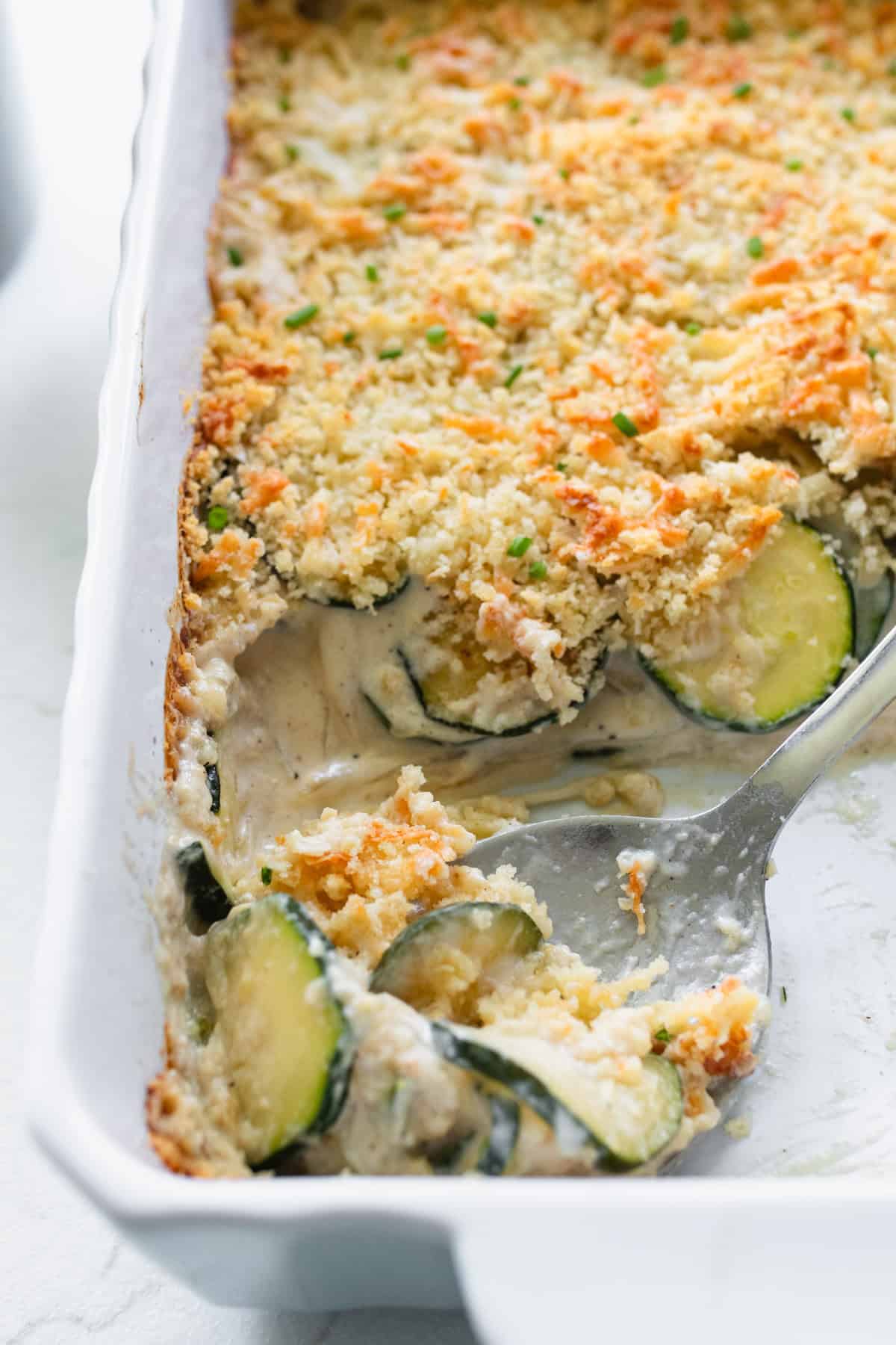 A large silver spoon scooping out zucchini gratin from a casserole dish.