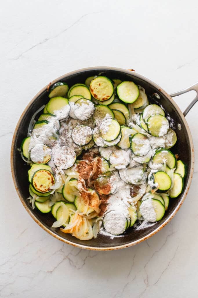 Seasonings added on top of coined zucchini in a skillet.