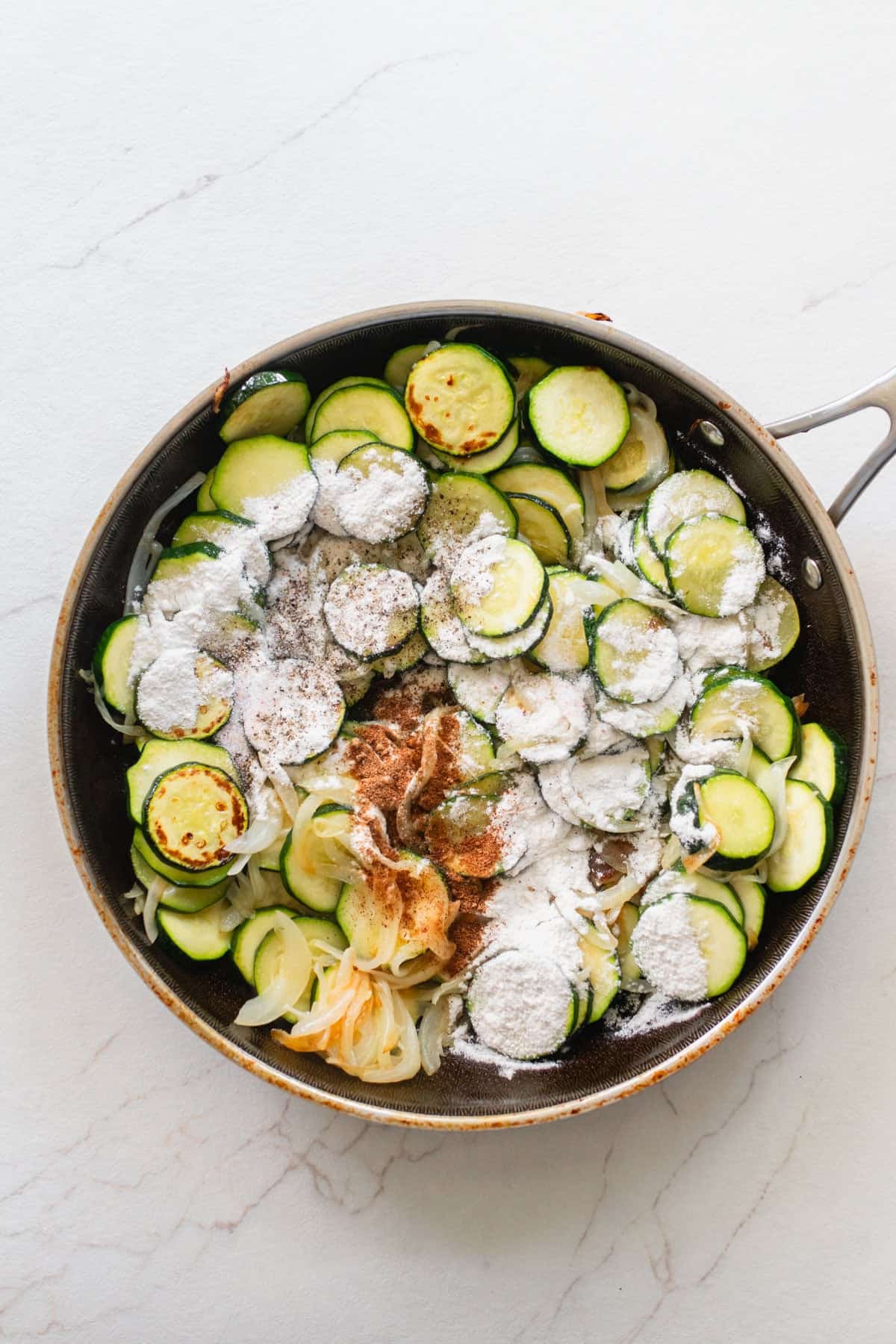 Seasonings added on top of coined zucchini in a skillet.