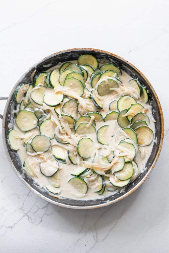 Cream sauce added to zucchini cut into coins in a skillet.
