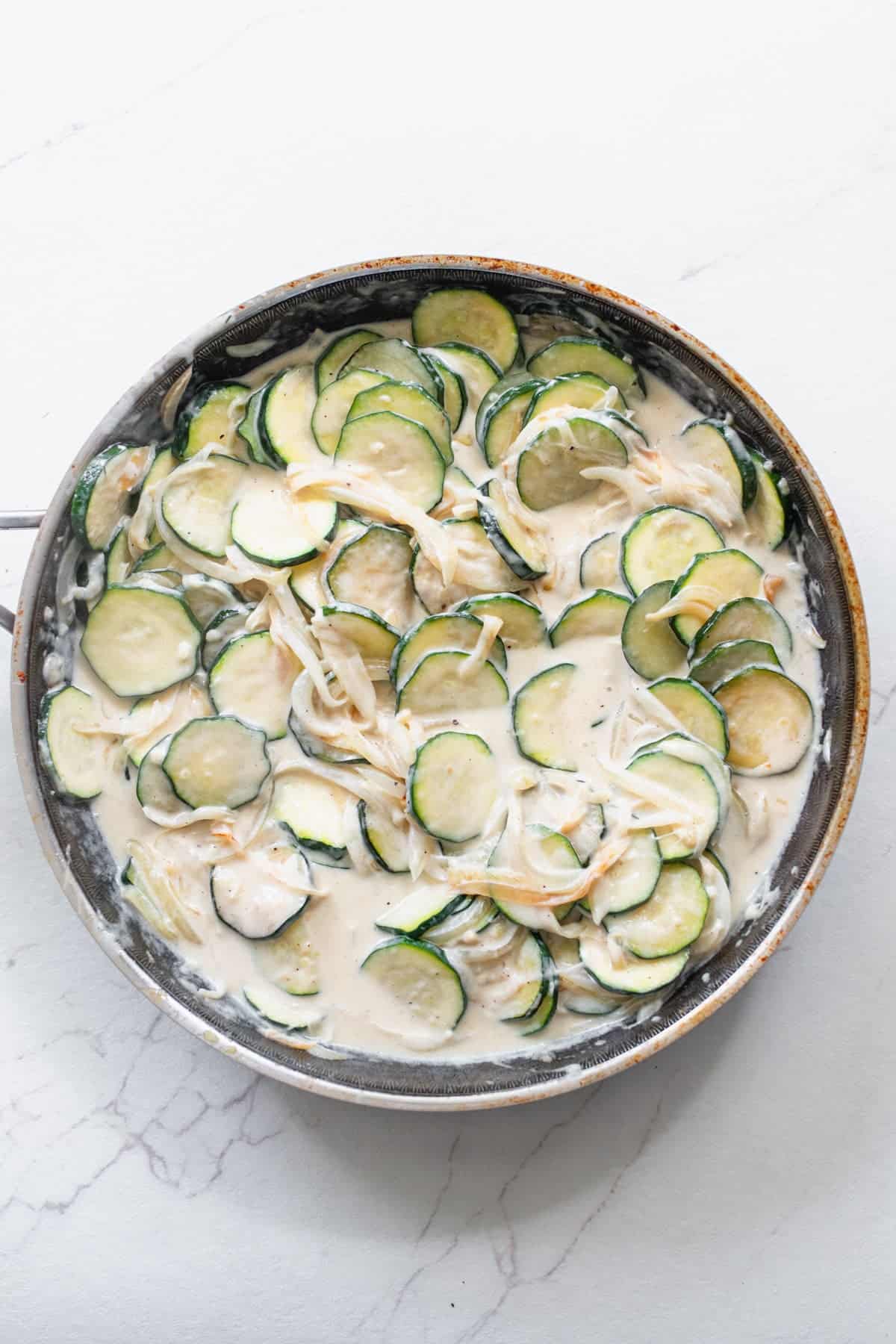 Cream sauce added to zucchini cut into coins in a skillet.