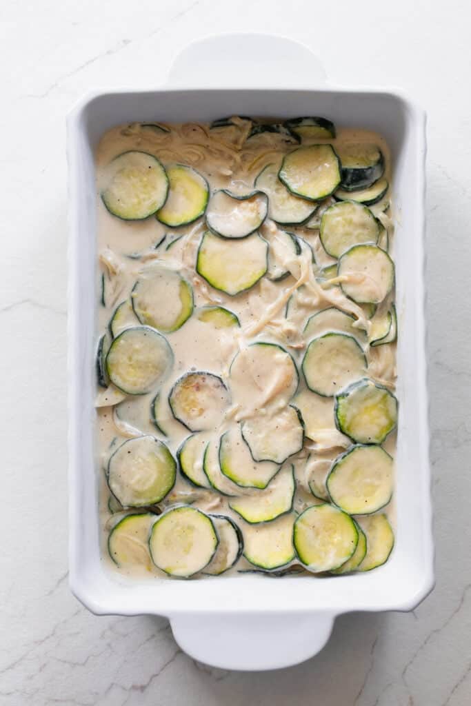 Zucchini cut into coins in a cream mixture in a casserole dish.