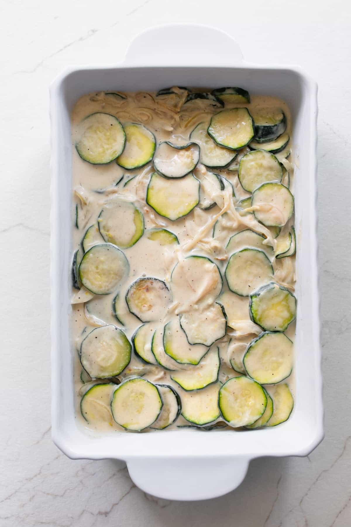 Zucchini cut into coins in a cream mixture in a casserole dish.