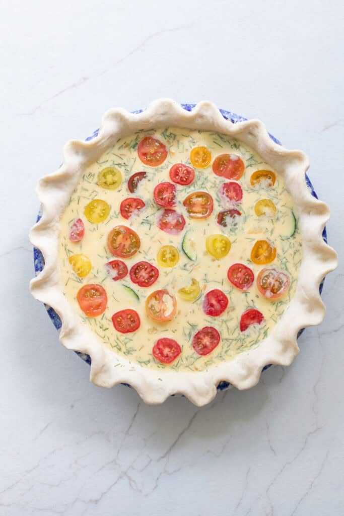 An egg mixture poured into a crust in a pie plate with cherry tomatoes on top.