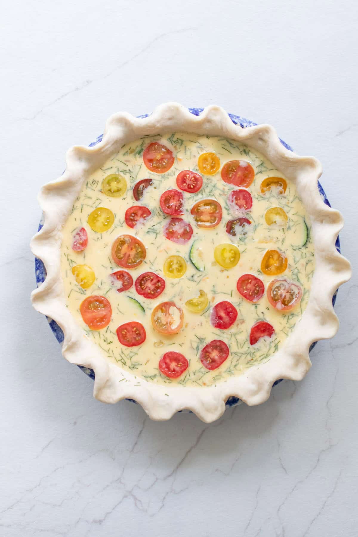 An egg mixture poured into a crust in a pie plate with cherry tomatoes on top.