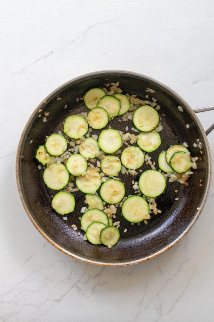 A skillet with zucchini rounds and onions.