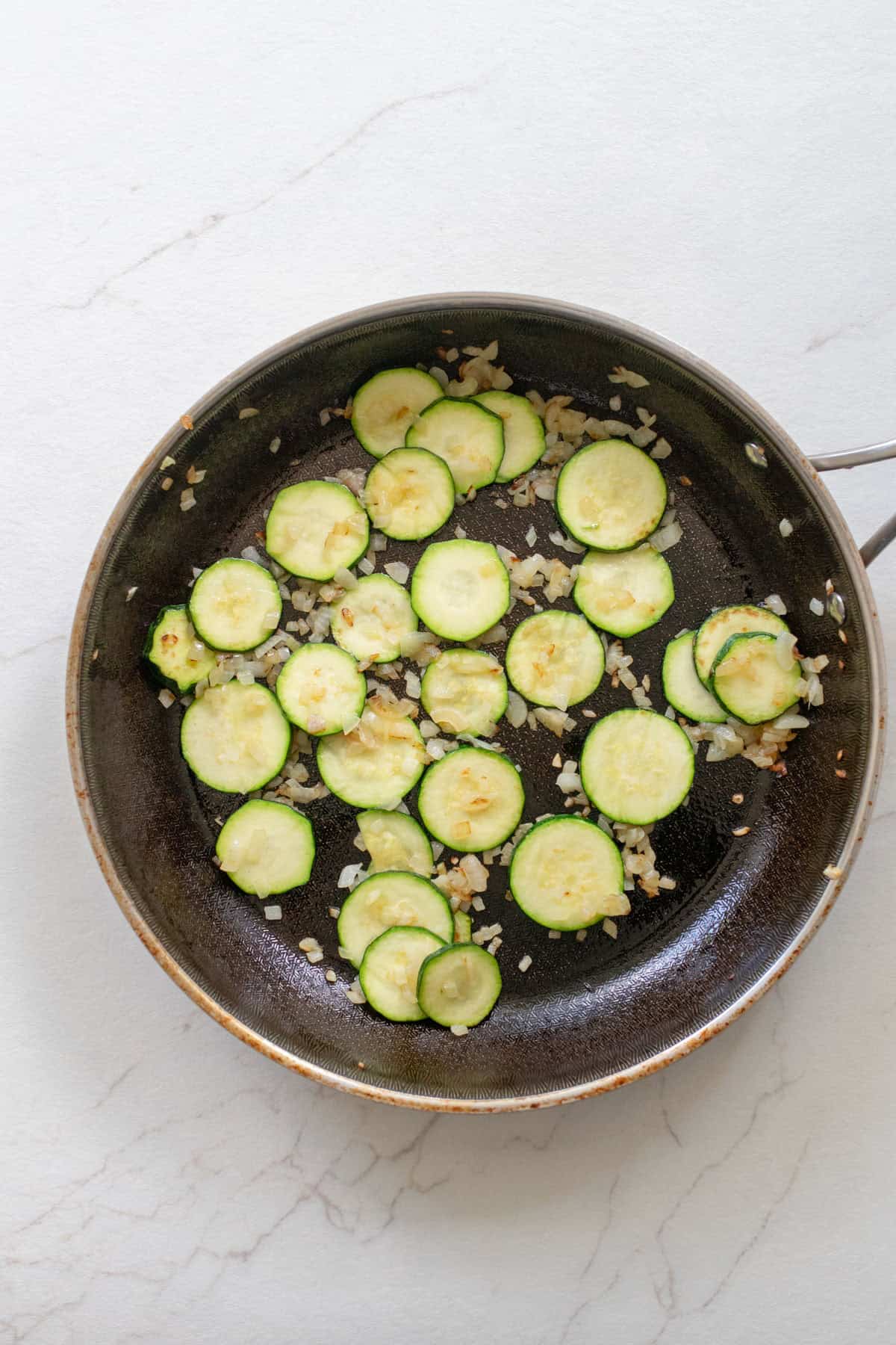A skillet with zucchini rounds and onions.