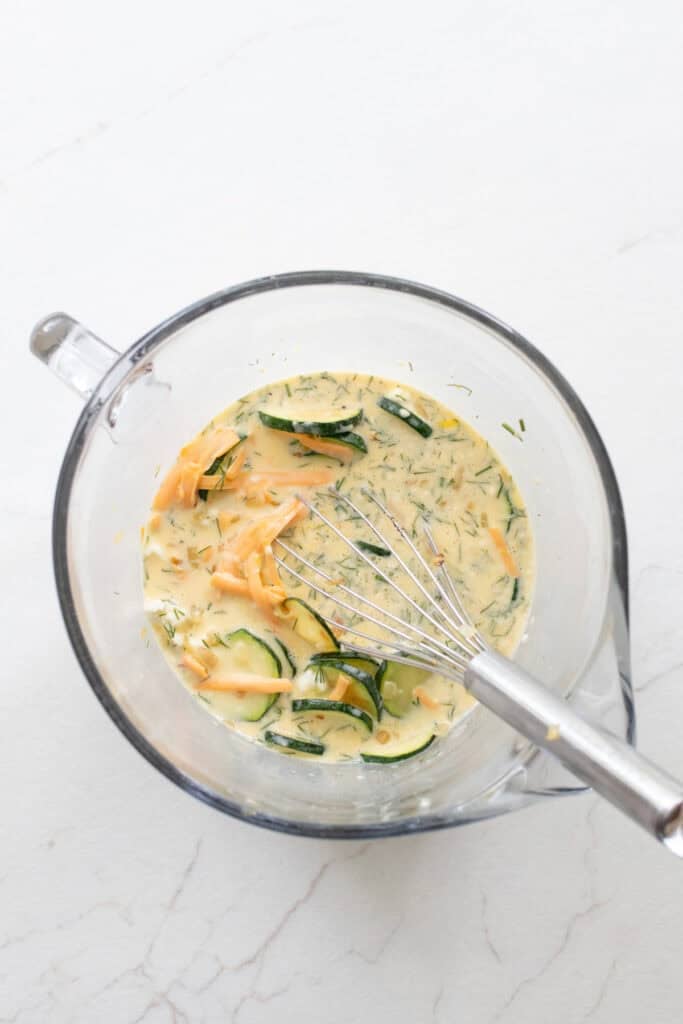 Ingredients added to a whisked egg mixture in a large glass measuring bowl.