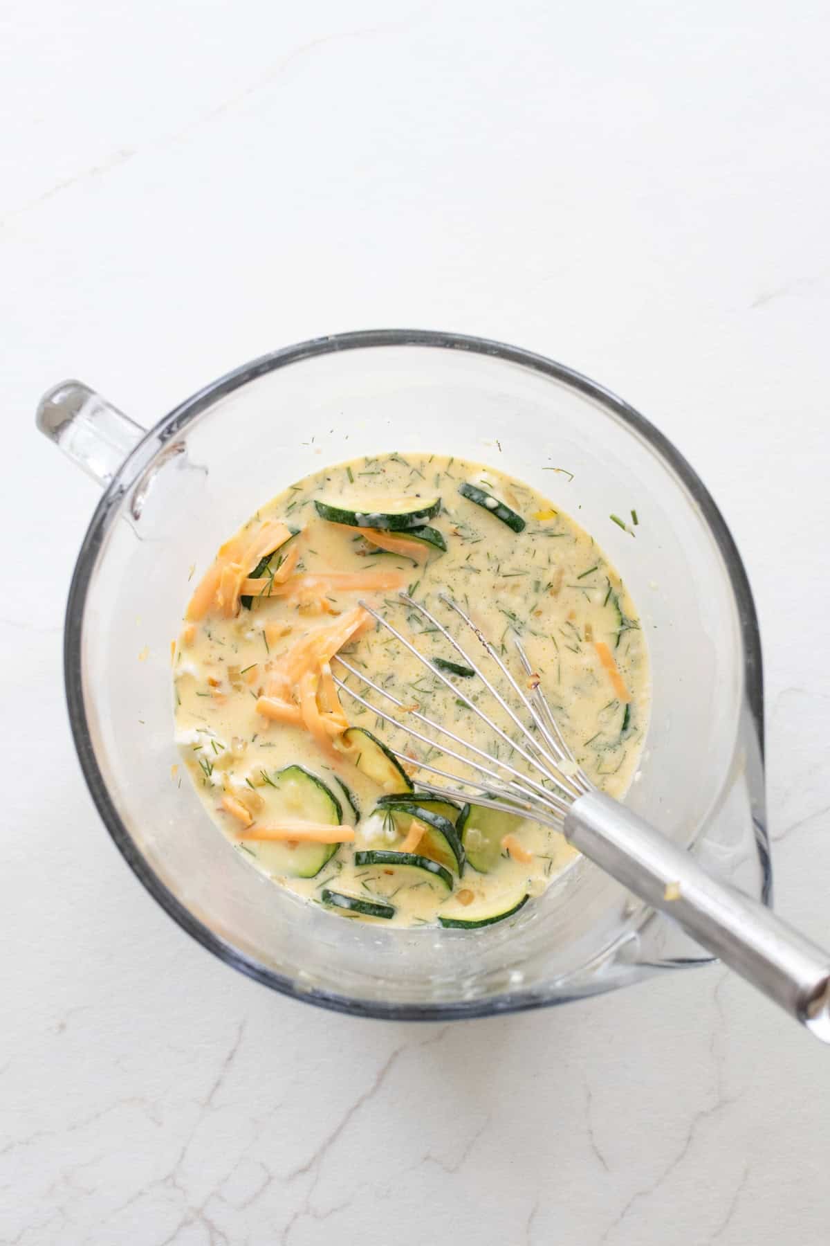 Ingredients added to a whisked egg mixture in a large glass measuring bowl.