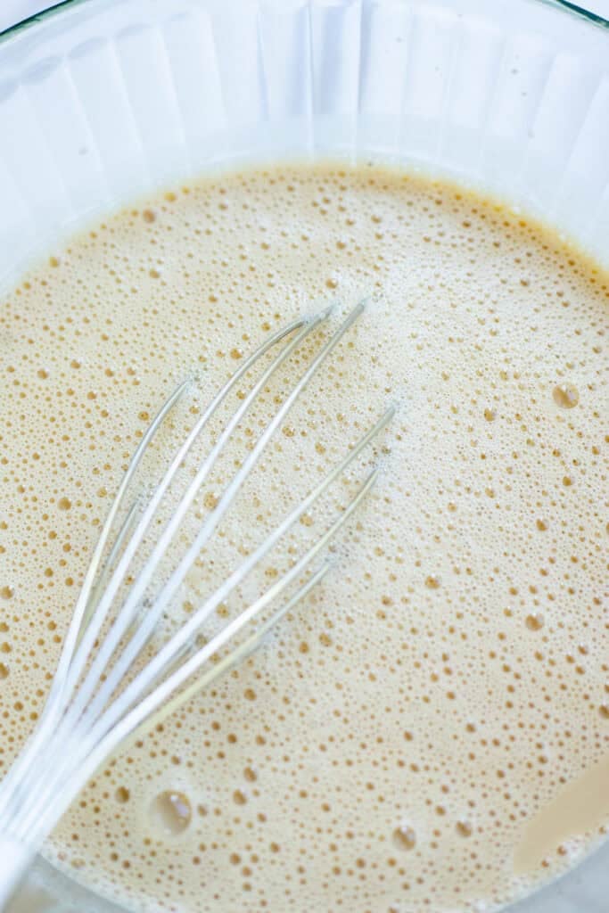Ice cream mixture in a glass bowl with a whisk.