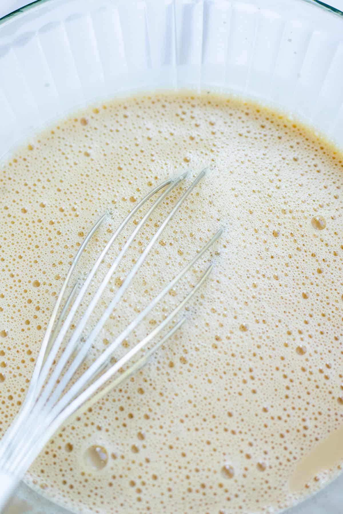 Ice cream mixture in a glass bowl with a whisk.