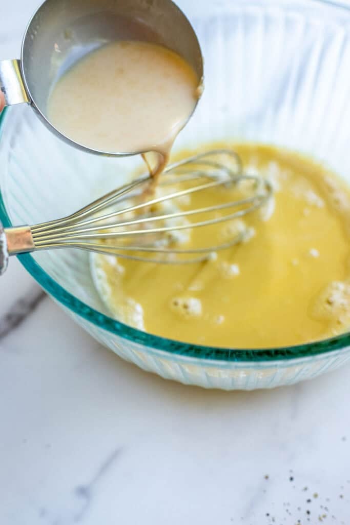 Hot milk mixture slowly added to the egg yolks in a glass bowl.