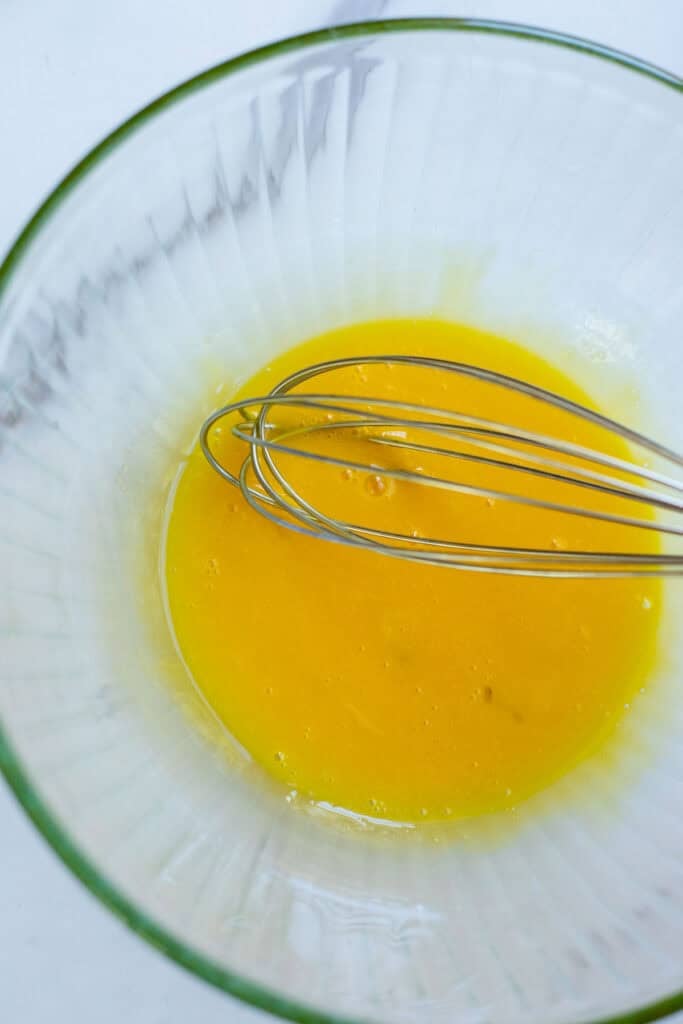 Egg yolks whisked into a glass bowl with a whisk.