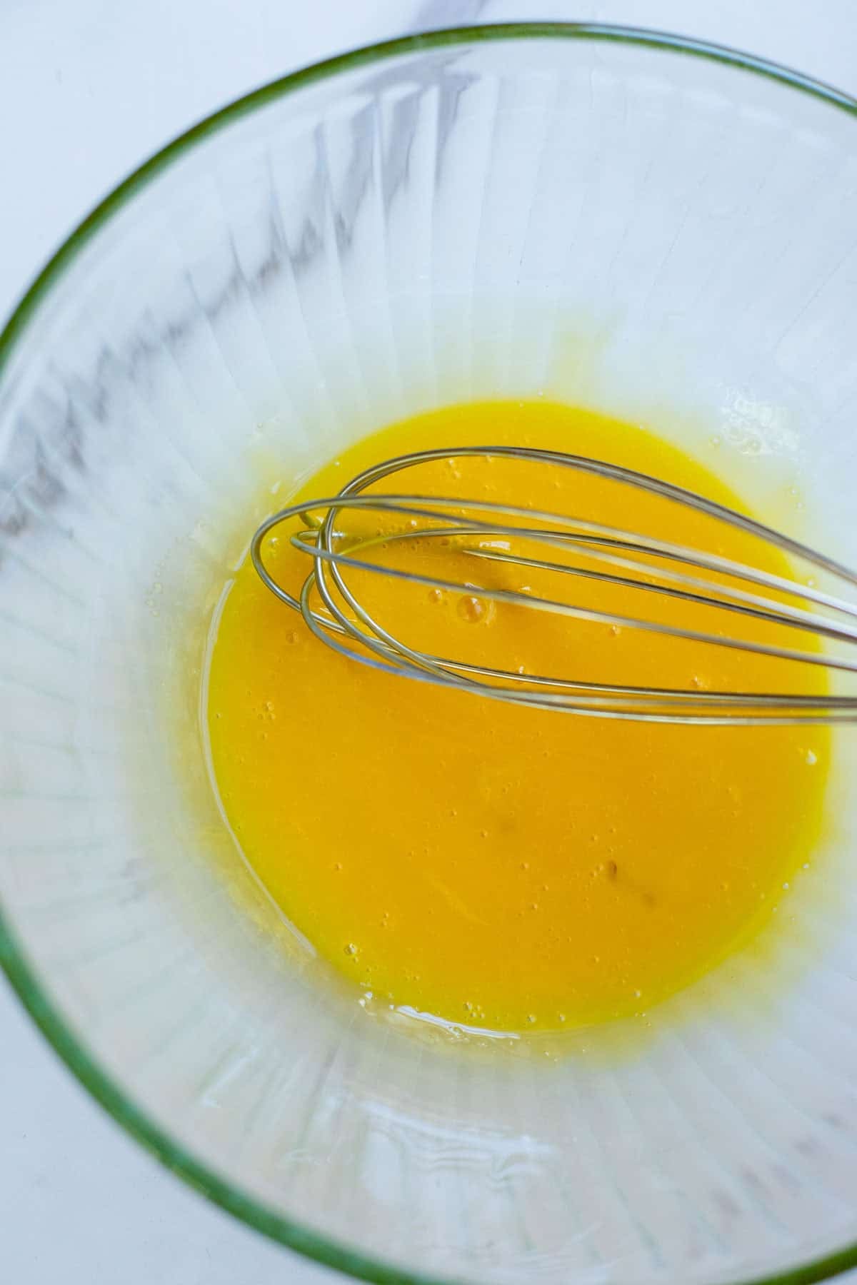 Egg yolks whisked into a glass bowl with a whisk.