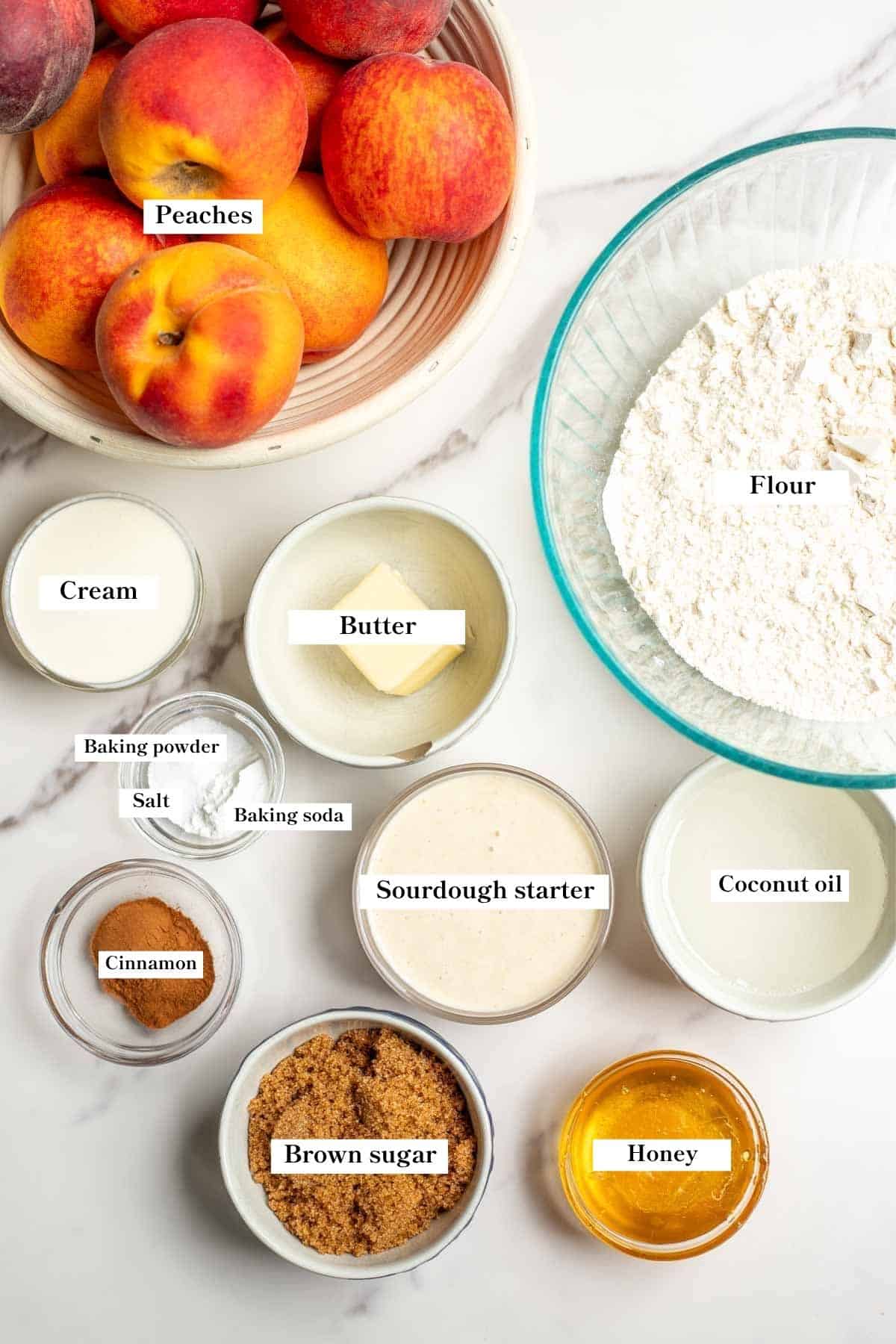 Ingredients for sourdough peach cobbler in dishes on a marble counter top.