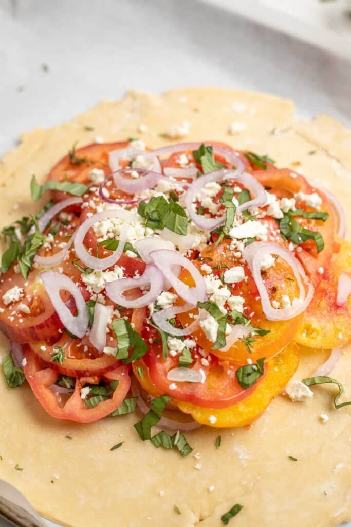 Sliced tomatoes, onions, feta, and herbs on a pie crust.