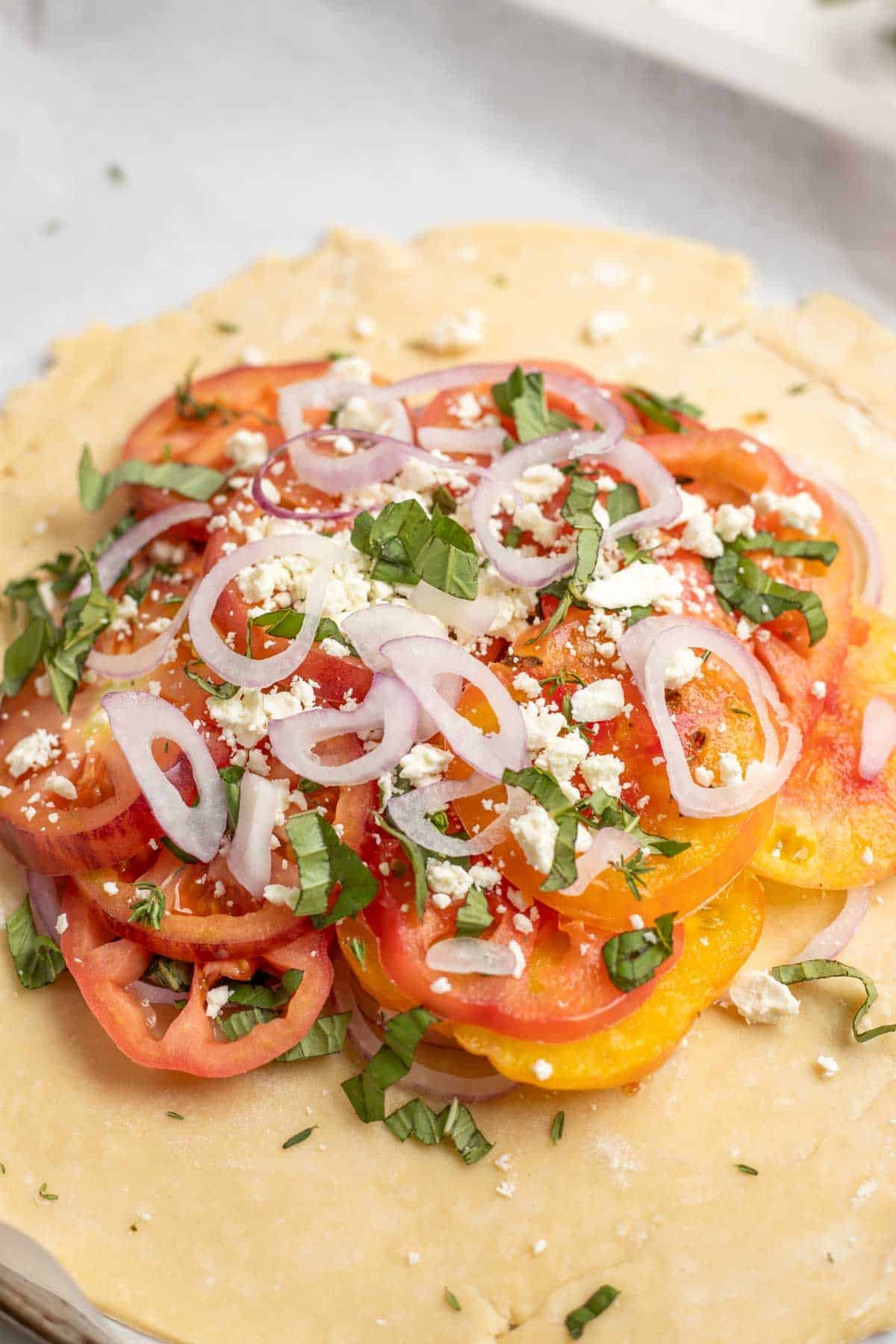 Sliced tomatoes, onions, feta, and herbs on a pie crust.