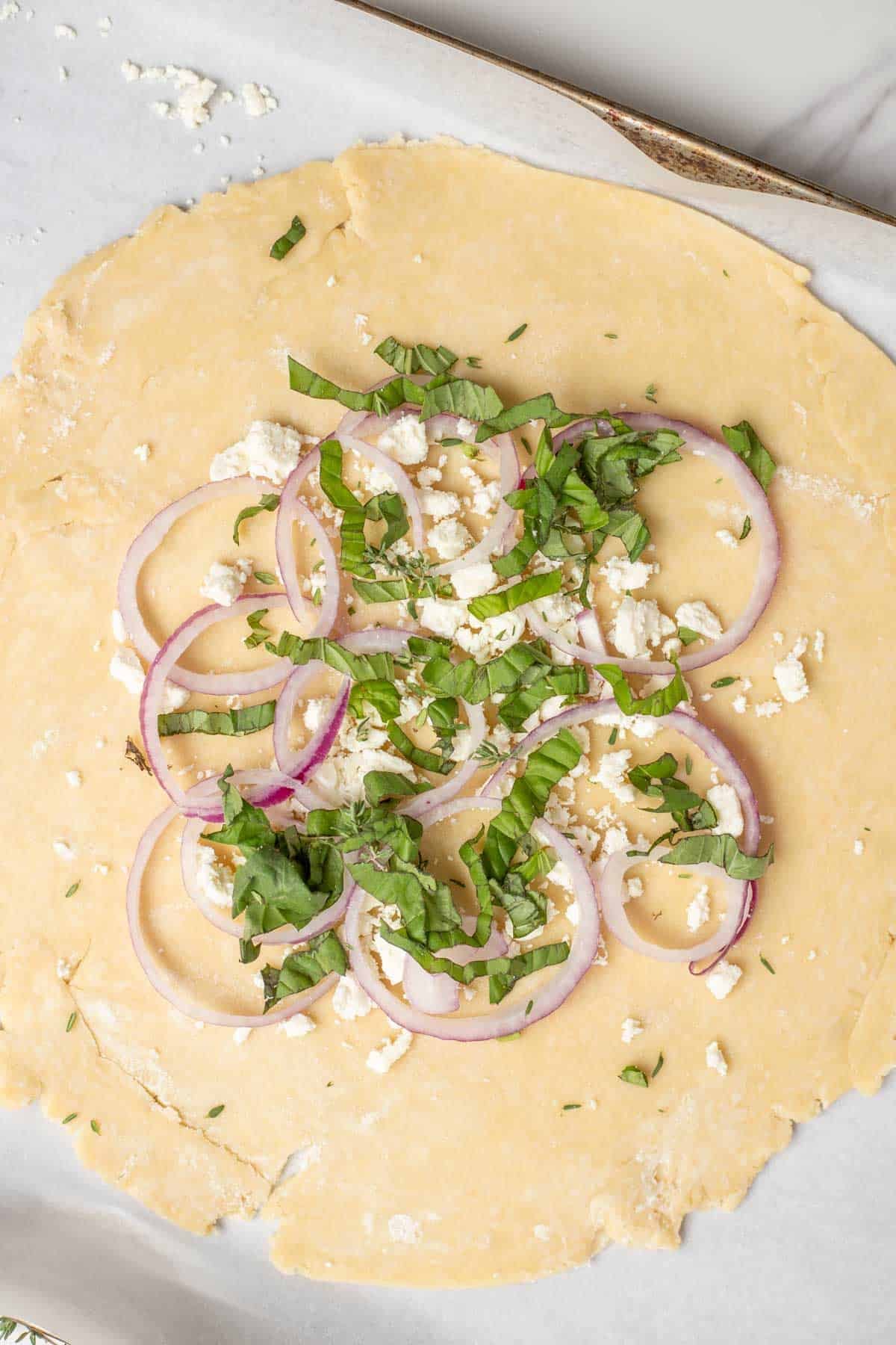 Basil, onions, and feta cheese spread evenly on a pie crust.