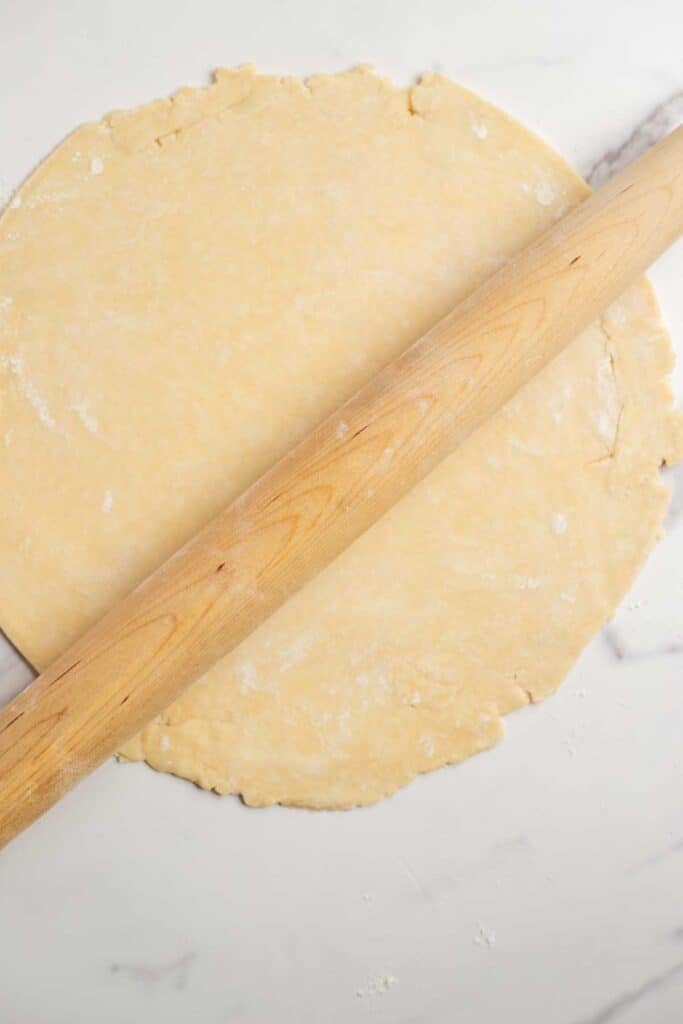 Aa pie dough rolled out with a rolling pin on a marble counter top.