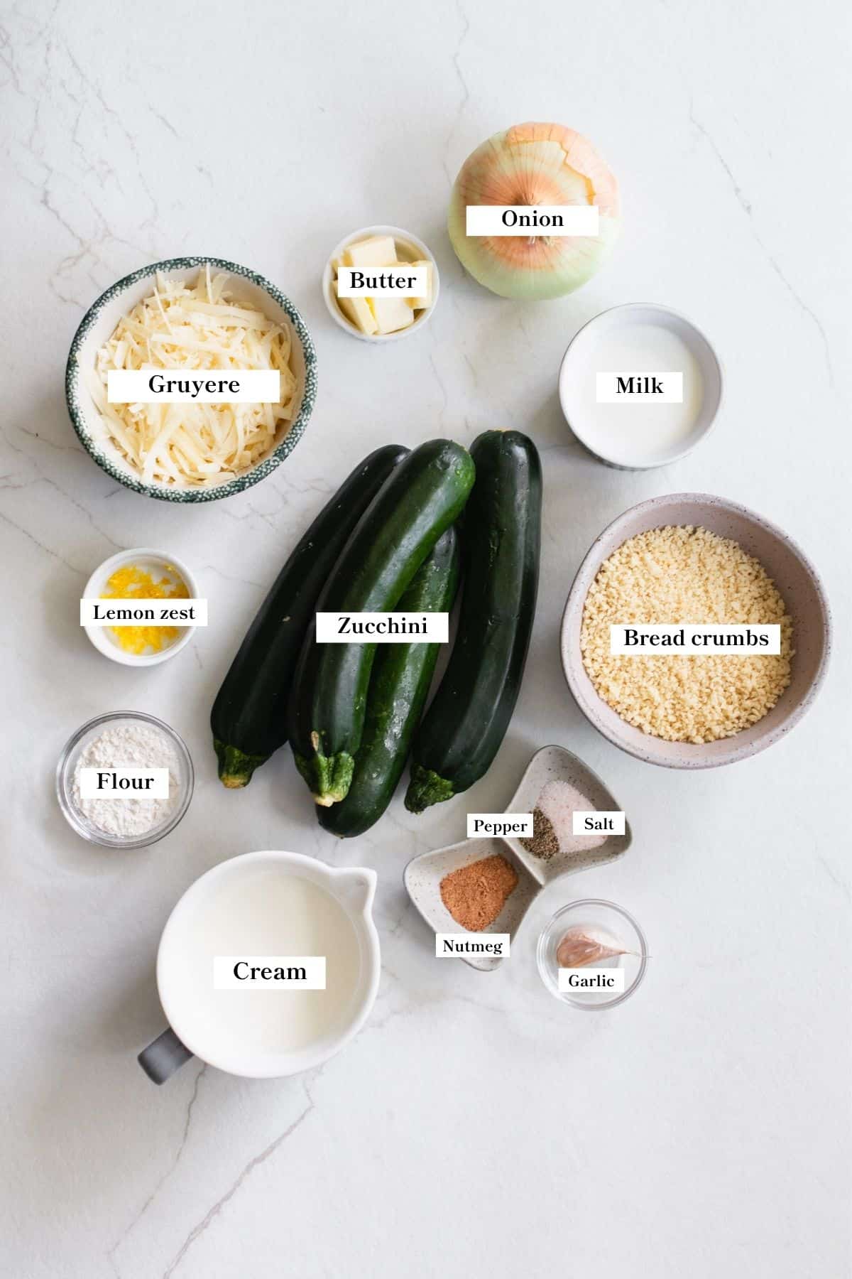 Ingredients for cheesy zucchini gratin in bowls on a counter top.