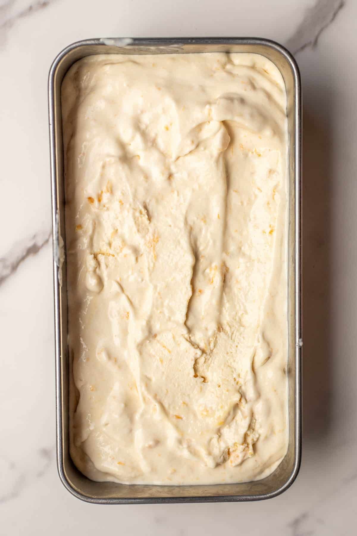 Peach ice cream added to a loaf pan to freeze.