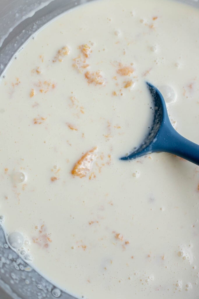 Milk, cream, salt, vanilla, and peach mixture in a bowl with a blue spatula.