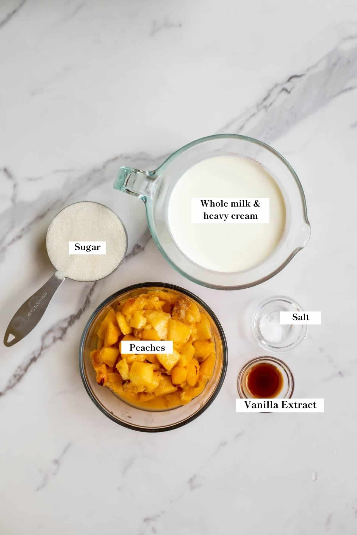 Peaches, cream and other ingredients in bowls on a white marble counter top.