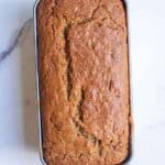 A baked loaf of zucchini bread in a loaf pan on a counter top.