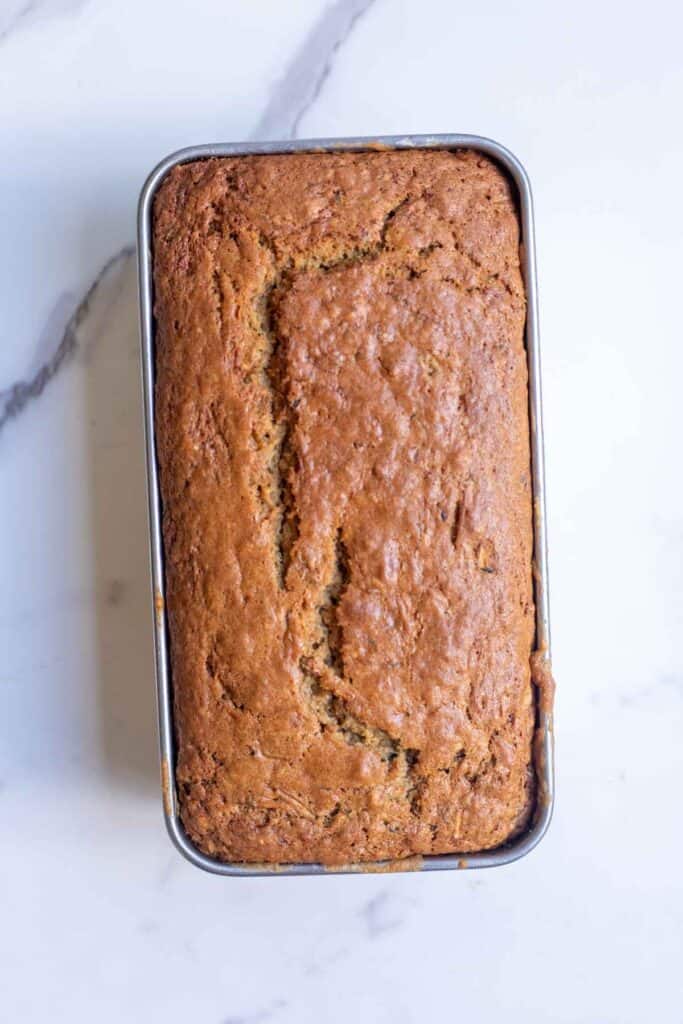 A baked loaf of zucchini bread in a loaf pan on a counter top.
