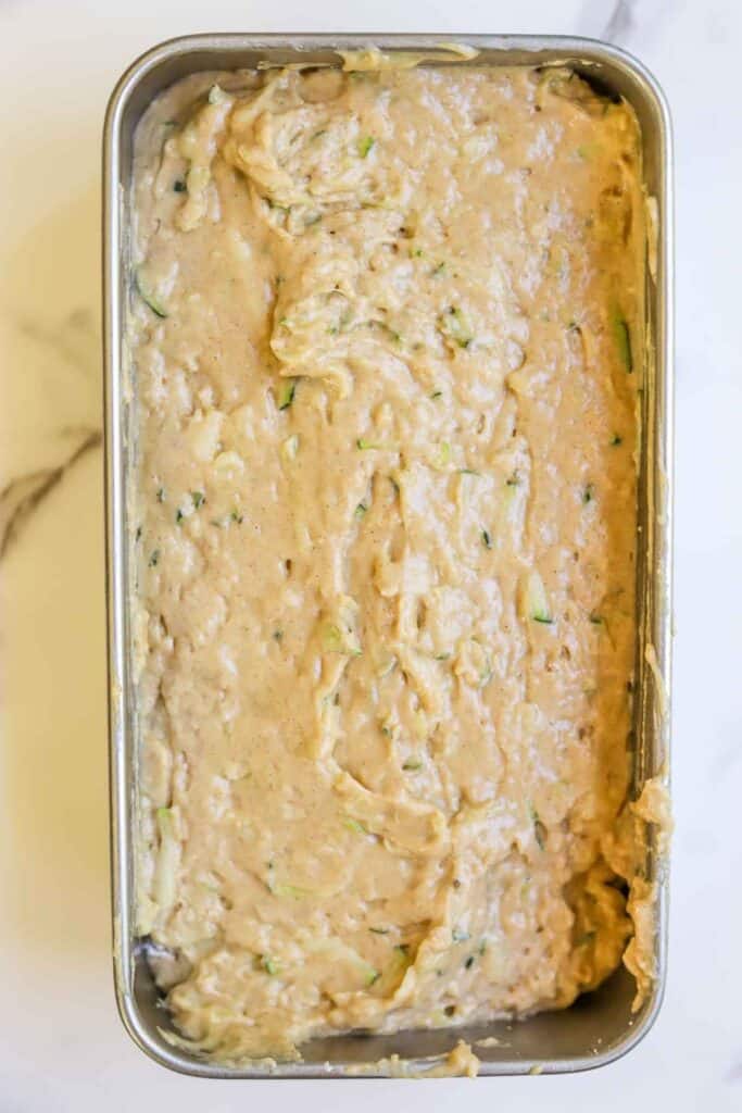 Sourdough zucchini bread batter in a loaf pan lined with parchment paper.