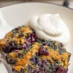 a slice of blueberry cobbler on a dessert plate with whipped cream.