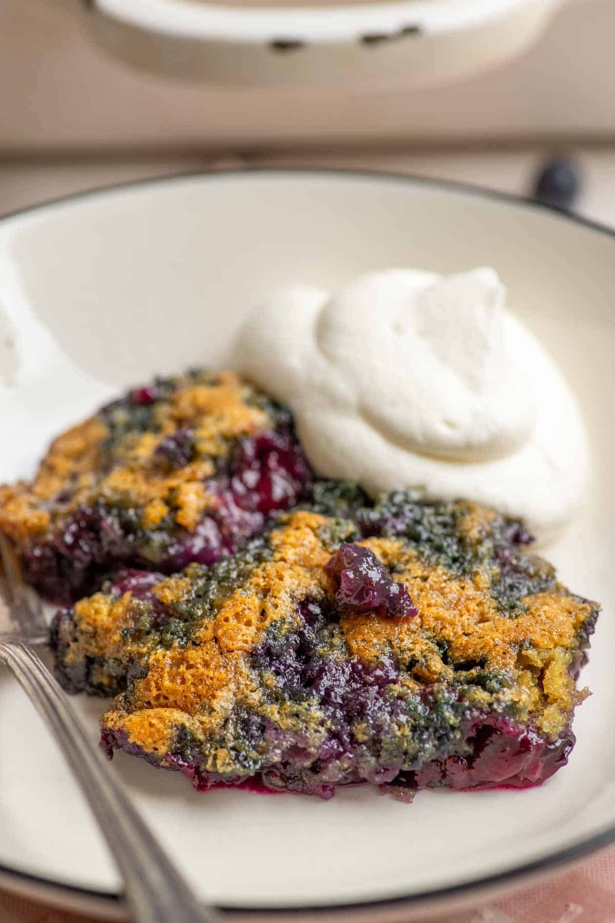 a slice of blueberry cobbler on a dessert plate with whipped cream.