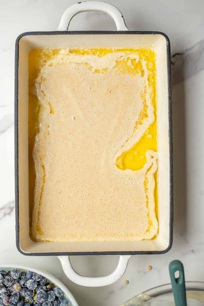 Cobbler batter added to a 9 by 13 inch dish coated with melted butter.