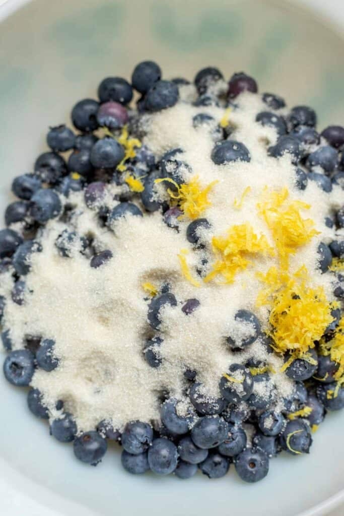Blueberries in a bowl tossed with sugar and lemon zest.