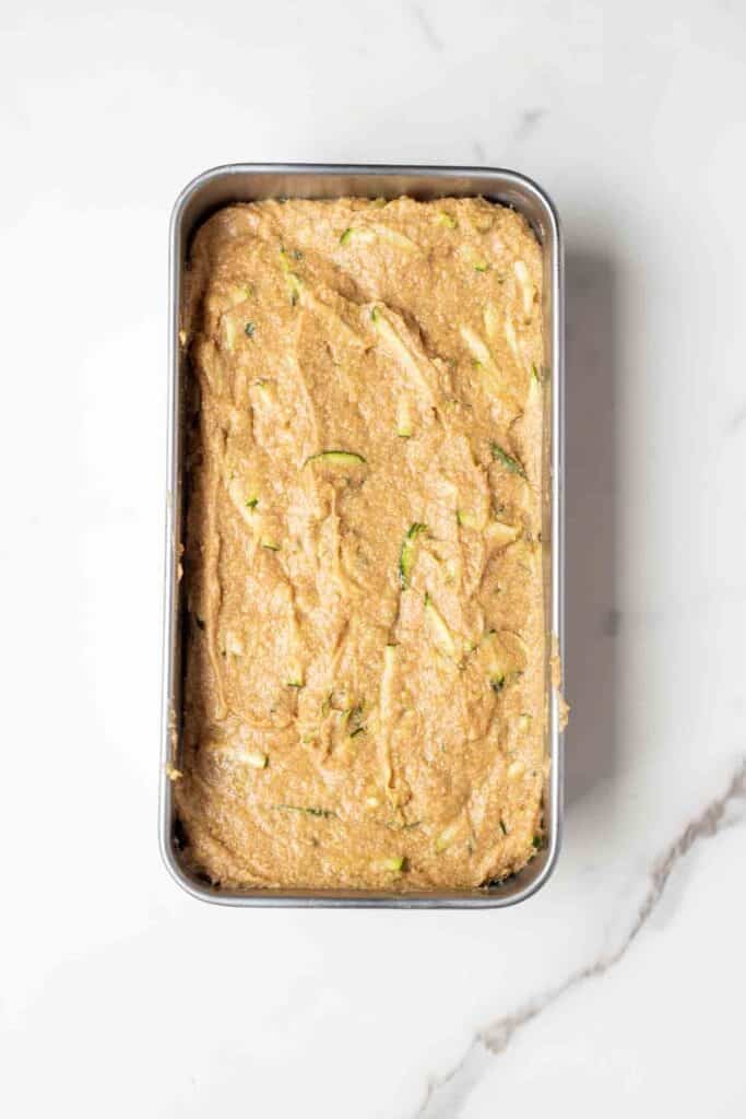 Zucchini bread batter poured into a loaf pan sitting on a counter top.