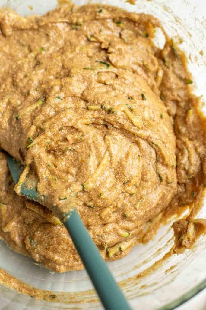 Wet ingredients folded together with dry ingredients in a glass bowl with a silicone spatula.