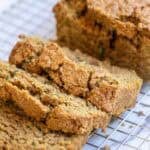 A loaf of zucchini bread with three slices cut out laying on a wire rack.